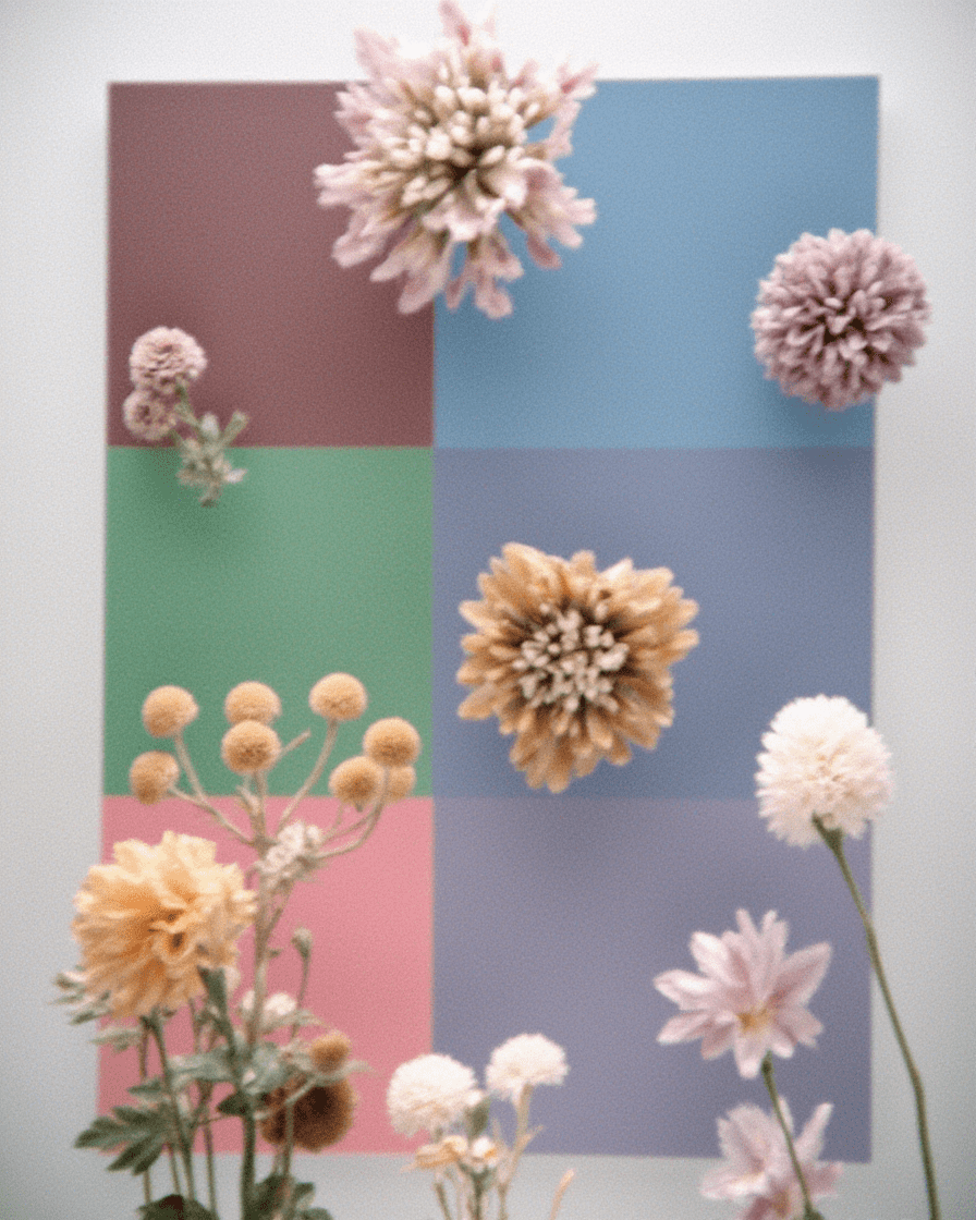AI-generated still life with dahlias and chrysanthemums floating over pastel color-blocked squares in mauve, blue, green, and pink