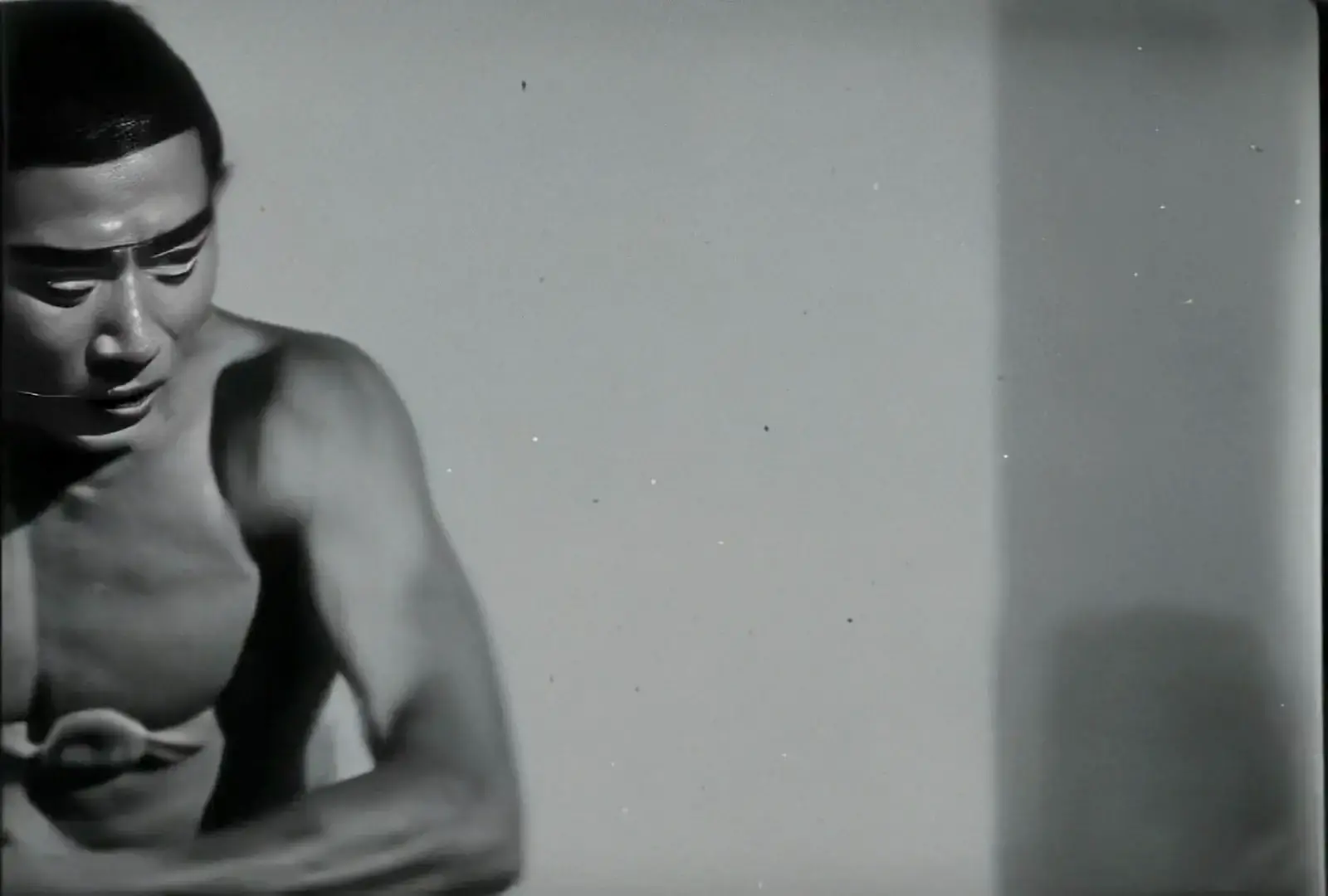 Shirtless figure in contemplative pose with grainy film texture and soft grey tones